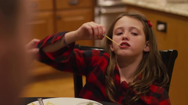 A girl dropping a spaghetti noodle in her mouth, eating dinner with her family