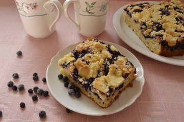 Grandma's homemade yeast cake made with frozen berries and crumble on white plate with two lovely mugs
