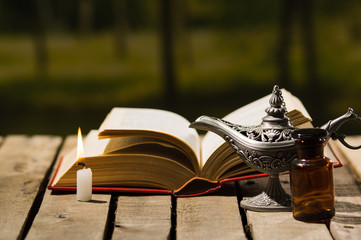 Thick book lying open on wooden surface, Aladin lamp and wax candle sitting next to it, beautiful...