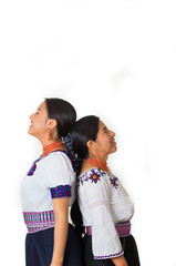 Beautiful hispanic mother and daughter wearing traditional andean clothing, both standing with backs rubbing against each other, seen from profile angle, white studio background