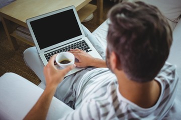 Father using laptop while having coffee in living room