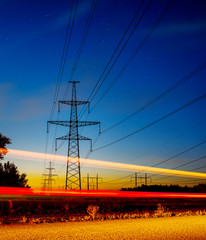 Long Exposure Red Car light trails on a road on blue hour with electrical power lines and pylons disappear over the horizon.