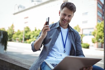 Fototapeta premium Handsome business executive holding mobile phone and laptop