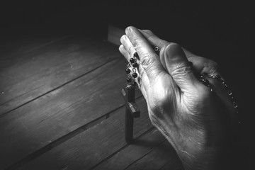 Hands holding rosary beads and cross while praying.