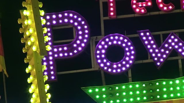 A close up of a carnival ride sign lit up at night.
