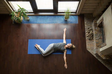 Attractive young woman working out in living room, doing yoga exercise on wooden floor, lying in...