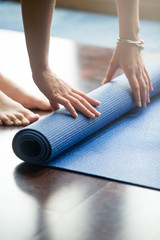 Close-up of attractive young woman folding blue yoga or fitness mat after working out at home in...