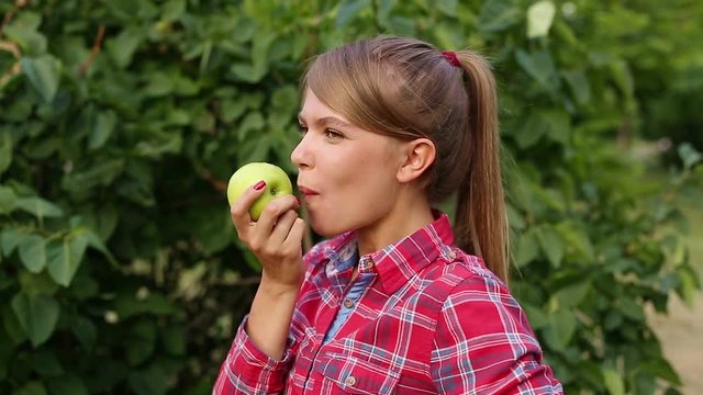 A young attractive girl eating a green apple in the park. Useful snack. Raw food diet and vegetarianism.