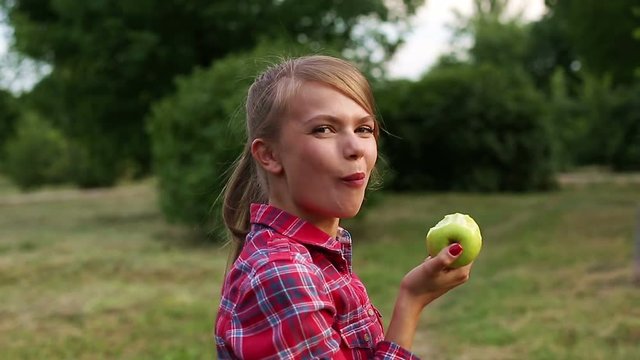 A young attractive girl eating a green apple in the park. Useful snack. Raw diet and vegetarianism.