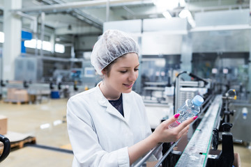 Young happy woman worker in factory checking robotic line for water bottling and packing....