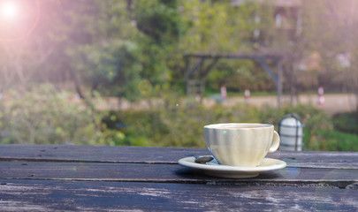 A cup of coffee on an old wooden table with a beautiful greenery