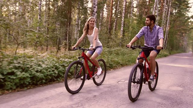 Portrait of happy couple having fun on bicycle ride in the summer park
