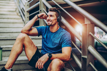 Handsome male jogger listening to music while taking break after morning training in urban setting