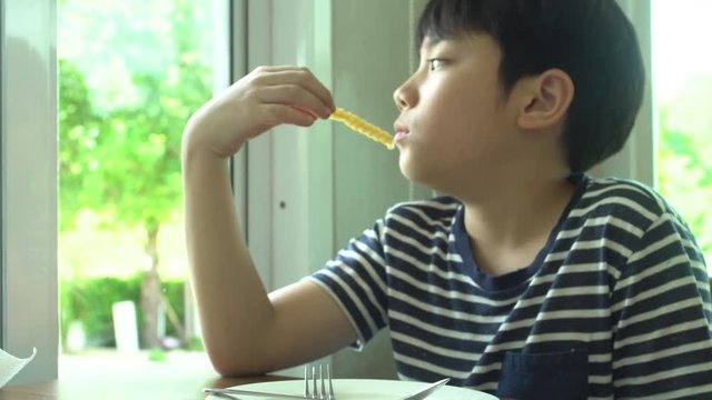 little Asian boy eating steak with vegetable Salad at restaurant with smile face