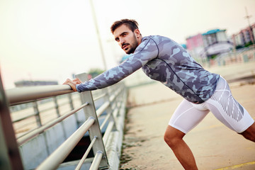 Male runner doing stretching exercise, preparing for sunset workout