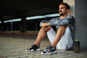 Portrait of a tired but satisfied with his training men runner resting after workout while sitting on concrete