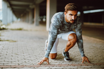 Fit and confident man in starting position ready for running. Male athlete about to start a sprint
