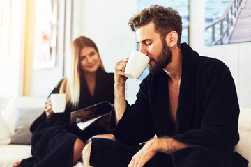 Happy young couple sitting on sofa in the bathrobe and drinking coffe in the morning