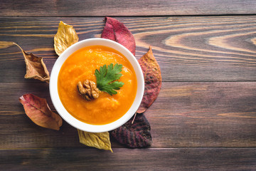 Orange vegan pumpkin soup on dry autumn leaves