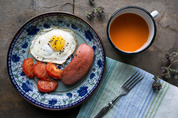 Simple breakfast. Fried egg with tomato and sausage on wooden table. Carrot juice. Top view