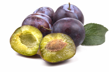 Four ripe blue plums two halves and green leaves
