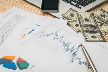 Fototapeta premium Financial charts on the table with laptop , phone ,dollars bankn