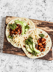 Spicy beans, avocado and green chile sauce tortilla on a rustic cutting board on a light background. Top view
