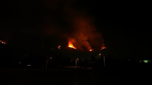 Three plumes of smoke rise from a distant fire overlooking a freeway.