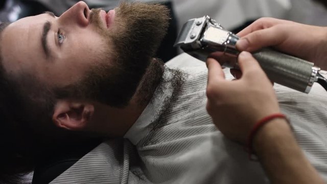 Hairstyling process. Close-up of a barber drying hair of a young bearded man