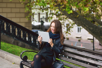 Young girl sitting on a bench , communication through the Internet , in the hands of the tablet.