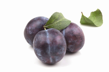 three large round ripe plums with leaves