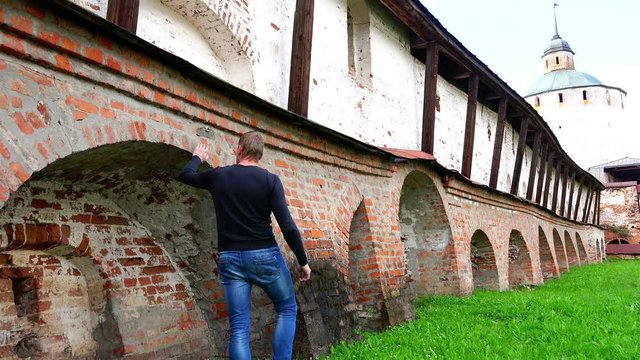 Tourist touches the historical reference massive brick walls of the monastery guarding against enemies