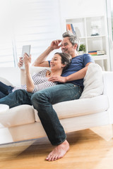Cheerful couple sitting on a white couch at home using a tablet