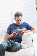  cheerful man at home using a tablet, he sits on a white couch