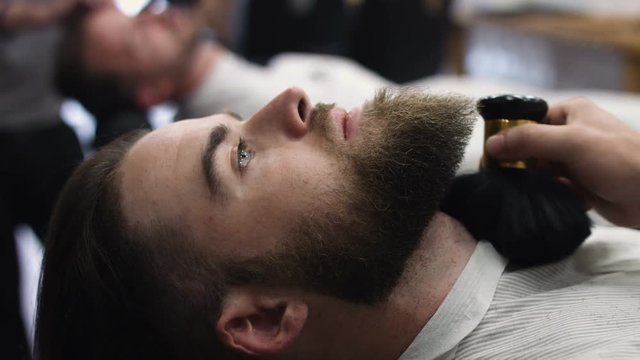 Hairstyling process. Close-up of a barber drying hair of a young bearded man