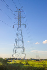 Electricity pylon silhouetted against blue sky wih cloud background. High voltage tower
