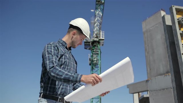 Builder stands with set of plan at the bulding under construction