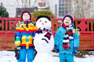 Two little siblings boys making a snowman