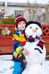 Funny kid boy in colorful clothes making a snowman