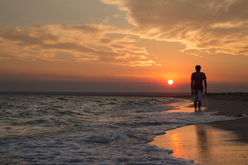 silhouette of a young man who walks on the beach, against the backdrop of a beautiful sunset