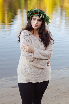 portrait of young brunette woman with a wreath of Rowan. Woman in autumn Park. Beautiful model posing near the water. Model plus Size, model form.