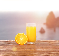 Tall glass of tasty freshly squeezed orange juice standing on an outdoor wooden picnic table on a hot summer day