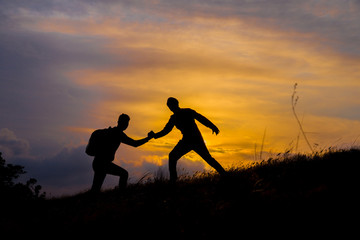 Teamwork couple hiking help each other trust assistance silhouette in mountains, sunset. Teamwork of two men hiker helping each other on top of mountain climbing team, beautiful sunset landscape.