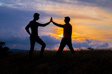 Fototapeta na wymiar Teamwork couple hiking help each other trust assistance silhouette in mountains, sunset. Teamwork of two men hiker helping each other on top of mountain climbing team, beautiful sunset landscape.