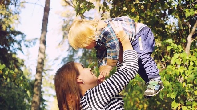 Young brunette mother lifting her son in park having fun enjoying motherhood on sunny autumn day in slowmotion. 1920x1080