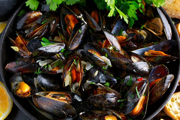 Boiled mussels in iron pan cooking dish. with herbs, butter, lime, parsley, garlic and fresh bread.