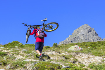 Mountainbiker trägt sein Bike über einen unwegsamen Gebirgspass