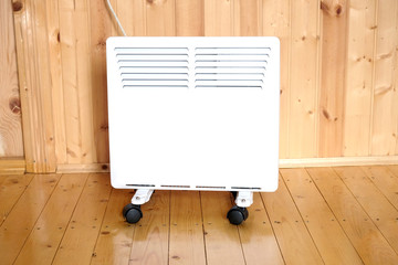 Working white electric convector heater plugged to power line in a wooden house room front view closeup