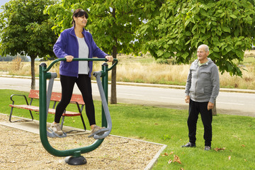  woman and elderly man exercising with  fitness equipment in public outdoor gym , selective focus
