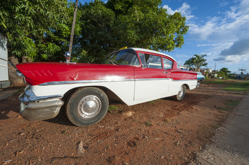 Vintage American car sits parked on a brown dirt driveway on the outskirts of Trinidad, Cuba